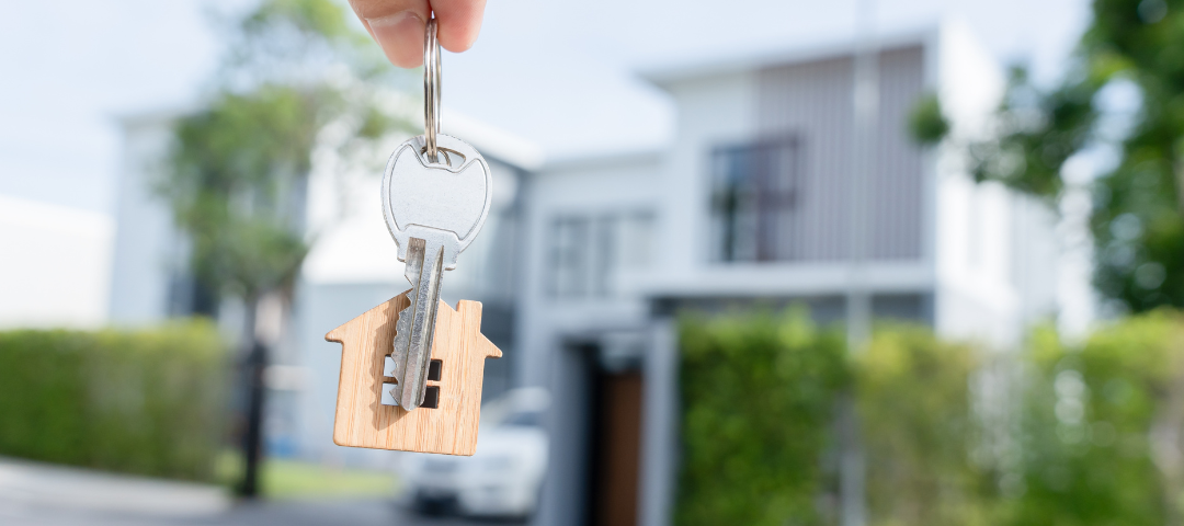 holding a house key with a new house as the background